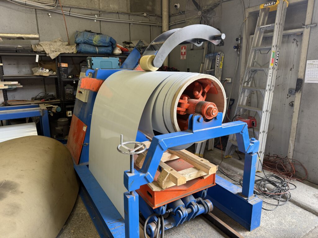 Stainless steel coil mounted on a decoiler machine feeding sheet material into fabrication equipment