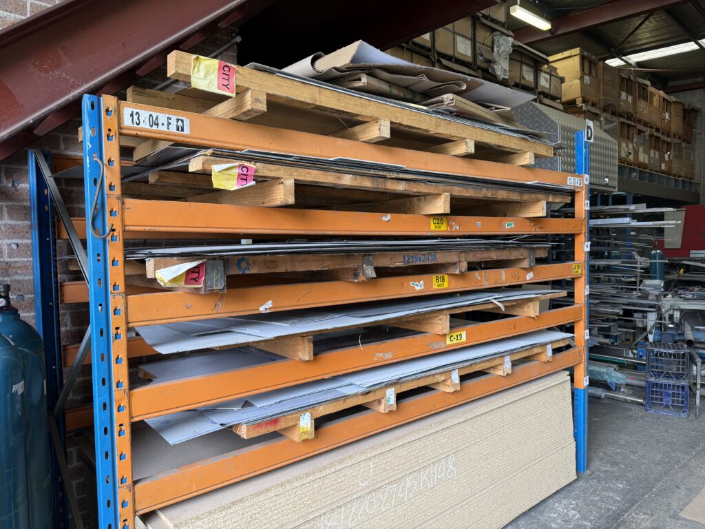 Stainless steel sheets stored on industrial racking in a fabrication workshop, showing standard flat sheet supply sizes